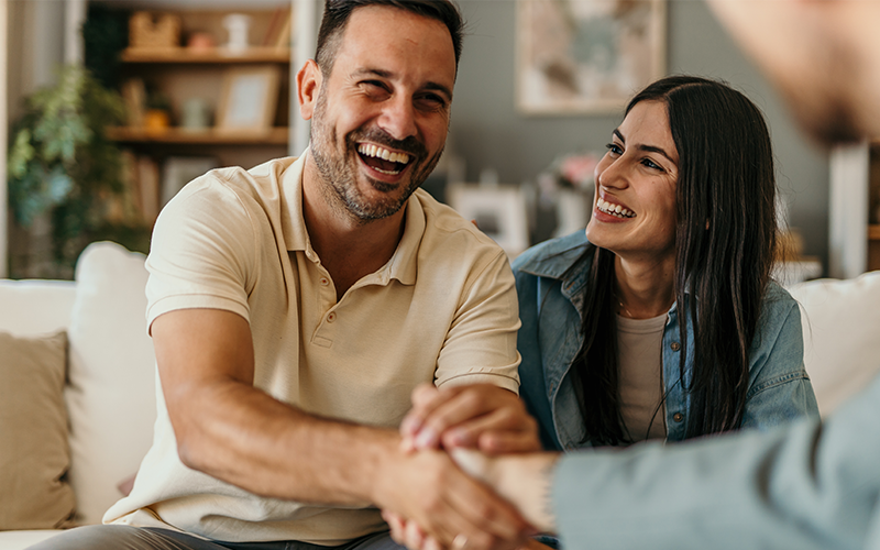 giovane uomo e giovane donna seduti sul divano, il ragazzo stringe la mando un una terza persona